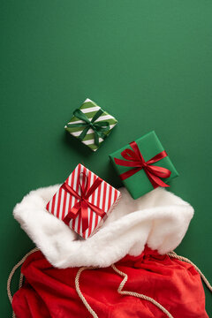 Merry Christmas Santa Claus presents in red velvet sack with wrapped gifts and bows for New Year on vertical green background