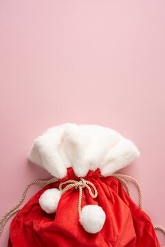 Merry Christmas Santa Claus sack with presents in red velvet and white fur for Happy New Year on vertical pastel pink backdrop