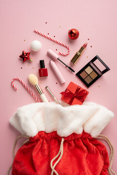 Merry Christmas and Happy New Year makeup gifts spilling from Santa Claus bag with candy canes and ornaments on vertical pastel pink background
