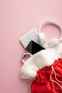 Santa present bag with headphones, keyboard and smartwatch for Merry Christmas and Happy New Year on vertical pastel pink background