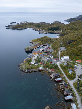 Aerial view of the Lofoten village with traditional red rorbuer cabins nestled along the rocky coastline, calm sea, and winding roads in Nordland, Norway.