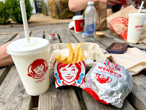A burger, fries and fizzy drinks meal bought from a Wendy's restaurant and eaten outside at a wooden picnic table