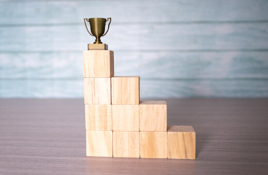 Step-by-step career progression concept, wooden blocks staircase with figure reaching for trophy