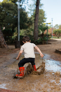 Child jumping splash playing in mud puddle