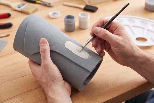 Person applying white glue or paint to gray foam cylinder with brush