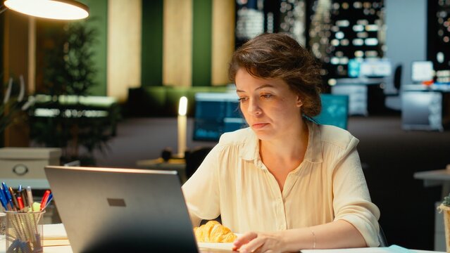 Corporate analyst eats unhealthy food while working late, using stress eating to cope with demanding after-hours work and emotional overeating at midnight.