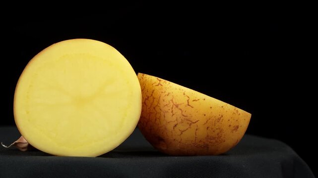 Camera dolly shot of fresh raw halved yellow potato on black background.