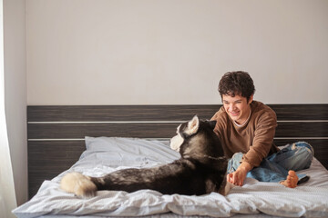 Happy teenage boy stroking his husky dog on the bed at home © iwavephoto