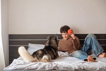 Teenage boy playing with a toy ball and his husky dog on a bed © iwavephoto