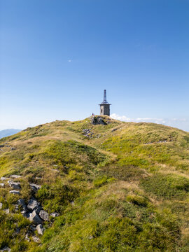 Aerial view of the Parco Nazionale dell'Appennino Tosco-Emiliano, featuring a stone structure on a grassy mountain peak under a clear blue sky, Massa e Carrara, Italy.