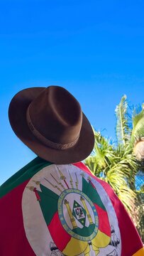 A hat on the head and the flag of Rio Grande do Sul (southern Brazil) across the chest, amidst nature and under a blue sky. Tradition, freedom, and pride in being a *ga&uacute;cho*. Farroupilha Week.
