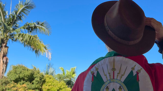 Holding a hat on their head and the flag of Rio Grande do Sul (southern Brazil) across their chest, amidst nature and under a blue sky. Tradition, freedom, and pride in being *ga&uacute;cho*. Farroupilha Wee