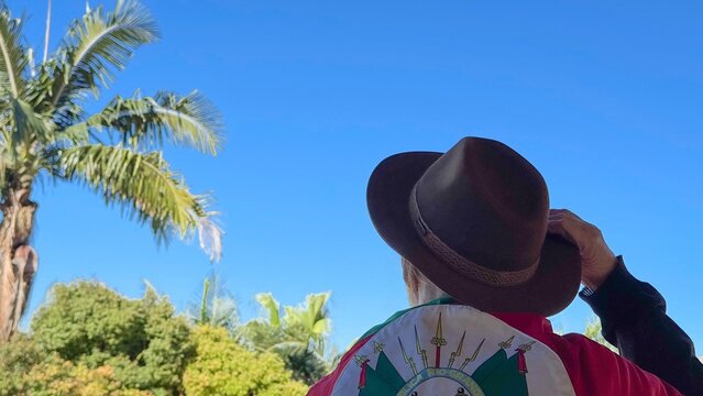 Holding a hat on their head and the flag of Rio Grande do Sul (southern Brazil) across their chest, amidst nature and under a blue sky. Tradition, freedom, and pride in being *ga&uacute;cho*. Farroupilha Wee