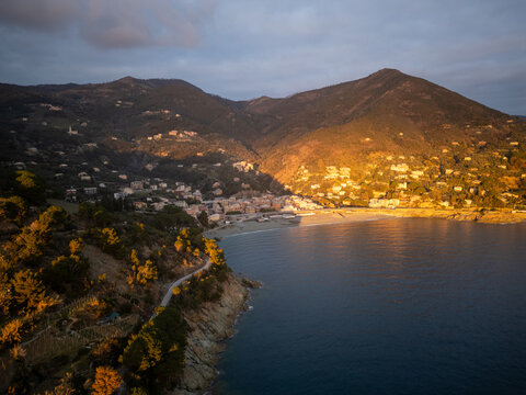 Aerial view of Cinque Terre coastline at sunset with golden light hitting the hills, terraced vineyards, and the Mediterranean Sea in La Spezia, Liguria, Italy.