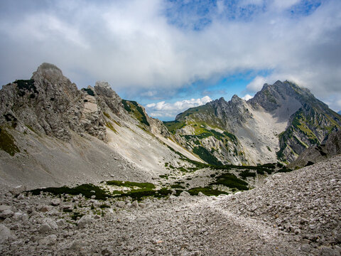 Wide high-angle view looking across a rocky scree field toward the alpine basin of Suho ru&scaron;evje, with the rocky ridge of Srednja peč and Mount Vrtača in the Karawanks, Slovenia