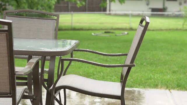 Rain falling on backyard patio furniture slow motion
