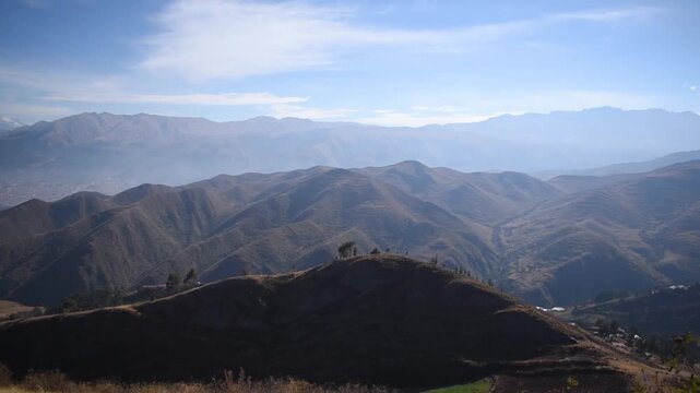 Panoramic view of mountains overlooking a distant city against a cloudy sky in Cusco, Peru.
