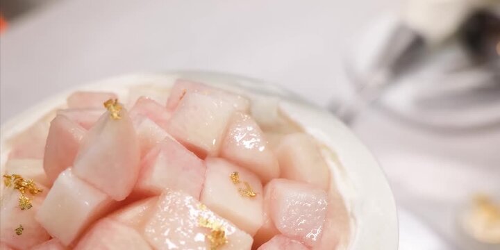 A macro, close-up stock footage shot showcasing a professional pastry chef wearing protective gloves using a delicate toothpick tool to meticulously apply flakes of shimmering, luxurious edible gold l