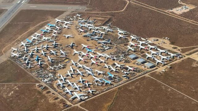 Aerial view of a large aircraft boneyard or scrapyard at an airport in the California desert, with many retired commercial airliners waiting for parting out or total destruction.