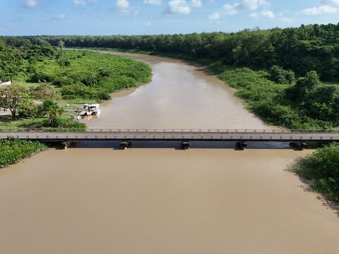 Aerial drone view of a bridge crossing a wide muddy river in Iracoubo, French Guiana, surrounded by tropical rainforest.