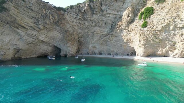 Aerial forward shot toward boats showing turquoise water and bright white cliffs at Chomi Beach in Corfu