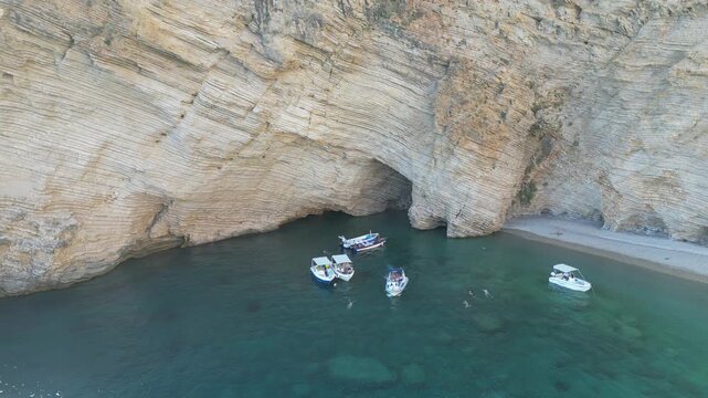 Aerial fly‑away from boats showing turquoise water and limestone cliffs at Chomi Beach in Corfu near Paleokastritsa