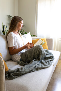 Female relaxing at home reading book enjoying herbal tea. Vertical.