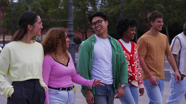 Diverse multicultural group young millennial friends walking hugging along urban street palm trees. University people laughing strolling outside on way to campus. Concept cheerful students together. 