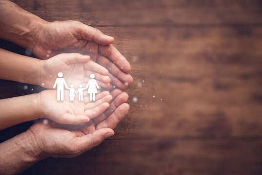 Adult and Child Hands Holding Glowing Family Icon on Wood Background for Life Insurance and Protection Concept