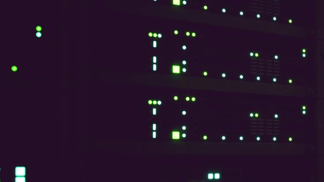 Multiple servers are placed in a rack inside a dark room. Green lights blink on the servers, indicating activity. The time is late at night when few people are present.