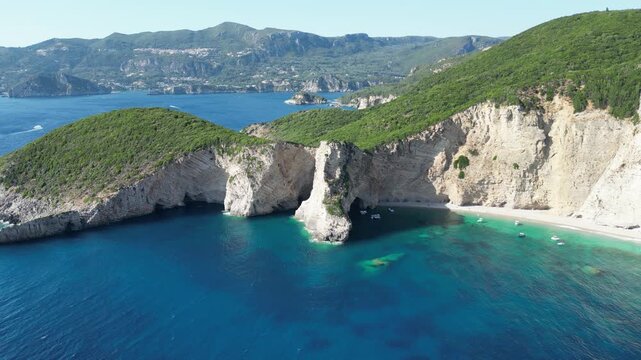 Aerial high‑angle static shot of Chomi Beach with turquoise water, anchored boats, and white cliffs near Paleokastritsa, Corfu, Greece