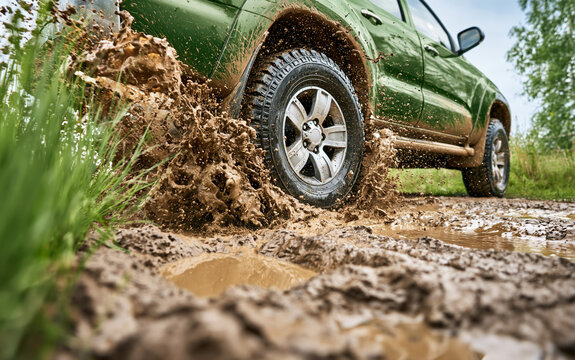 Low angle view of suv wheel driving through mud puddle on country road