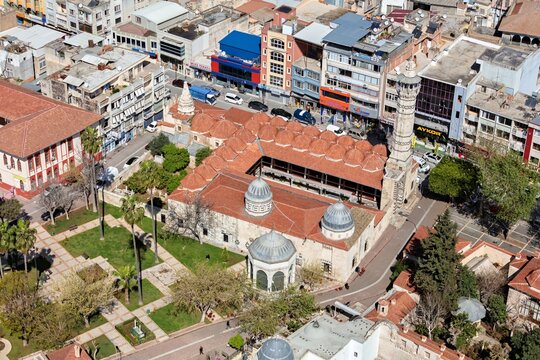 Aerial view of the historic Ulu Cami mosque with its distinctive red-tiled roof, minaret, and surrounding urban landscape in Adana, Turkey.