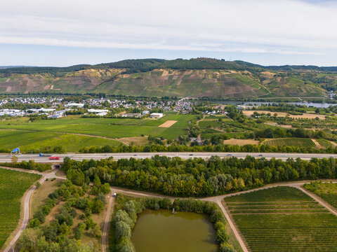 Aerial view of the Moselle valley landscape featuring lush vineyards, agricultural fields, a small pond, and the busy autobahn with traffic, Schweich, Rhineland-Palatinate, Germany.