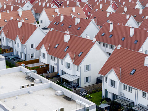 Aerial view of a modern residential housing development featuring rows of white houses with red tiled roofs and small private gardens in Poland.