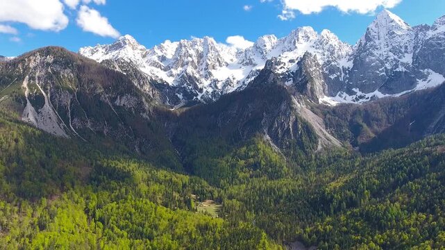 Aerial view of the snow-capped peaks of Triglav mountain range rising above dense green forests in Mojstrana, Jesenice, Slovenia.