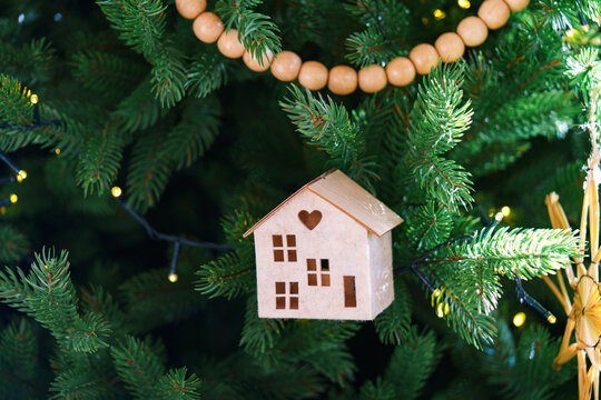 Handmade craft holiday Christmas ornaments on festive green spruce tree with warm glowing lights and natural wooden rustic aesthetic decor. Straw stars, small house, wooden garland and macrame details