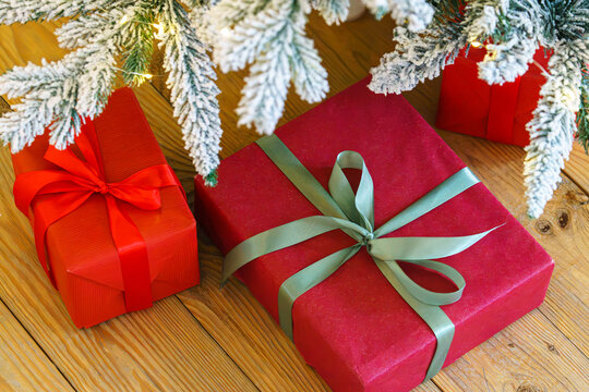 Beautiful presents, gift boxes wrapped in elegant red paper under green snowy festive Christmas tree with warm lights. Cozy winter holiday atmosphere perfect for seasonal celebrations and decor themes