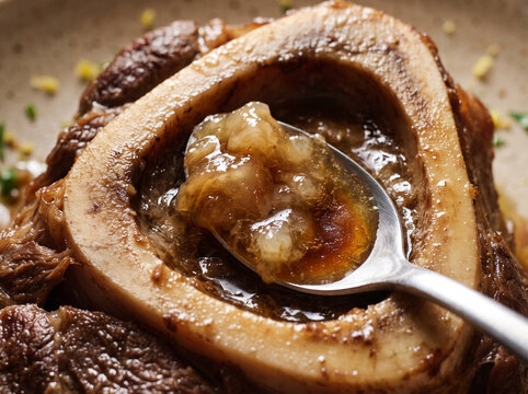 Macro shot of silver spoon scooping rich bone marrow from braised osso buco veal shank