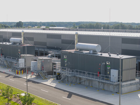 Aerial view of ai data center power generator system with industrial containers and cooling units installed next to a large warehouse facility in Poland.