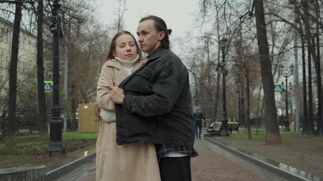 Close up of man and woman standing in outdoor park setting couple interacts with each other. scene shows them facing forward initially then moving closer together as they embrace revealing