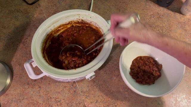 Ladling hot chili from slow cooker into bowl
