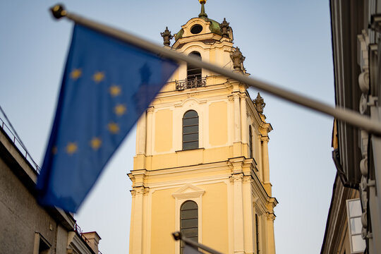 European Union flag in front of the bell tower of the Church of St Johns in the historic center of Vilnius, Lithuania. European architecture illuminated by warm evening light.
