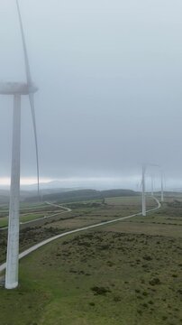 Aerial view of wind turbines at Parque eolico Neda in foggy conditions with rolling hills and access roads in Lugo, Lugo, Spain.