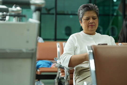 An elderly woman with her suitcase dozes off with her hand on the luggage handle in a bright airport waiting hall, a candid moment of solo travel, an authentic look at ageing and technology