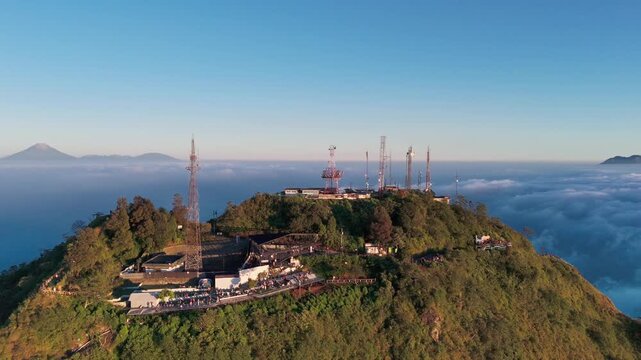 Aerial view of Mount Telomoyo summit with communication towers above a sea of clouds at sunrise in Kecamatan Ngablak, Jawa Tengah, Indonesia.