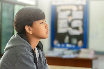 Naklejka premium Sad and lonely teenage boy in a grey hoodie sitting in a classroom, looking away with a depressed expression, feeling isolated or bullied.