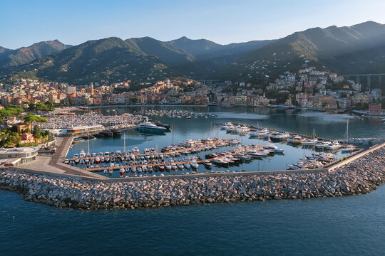 Aerial view of the marina in Rapallo filled with numerous yachts and boats, protected by a stone breakwater, with the coastal town and mountains in the background Rapallo, Liguria, Italy.