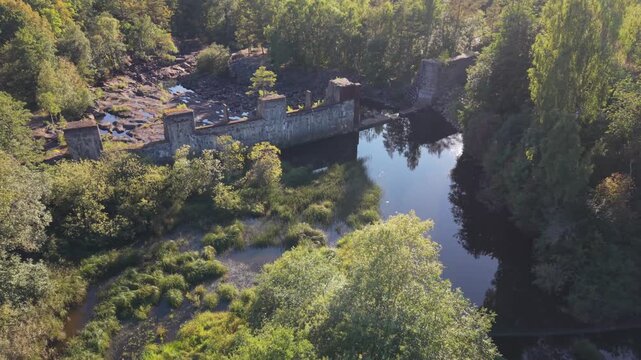 Aerial view of the historic Yngeredsfors Doda Fallet powerplant ruins surrounded by lush forest and the river in Vessigebro, Hallands lan, Sweden.