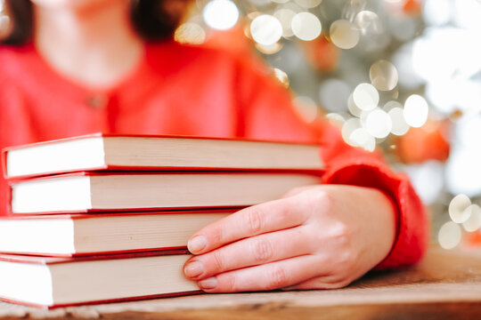Holiday Reading Books.Woman Reading Books During Christmas Winter Holidays.hardcover books beside a glowing Christmas tree for bookstore advertising, library events, winter reading 